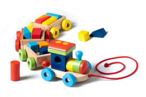 A wooden toy train carrying puzzle pieces as cargo, painted in many colors, pulled by a red string. Isolated on white background.